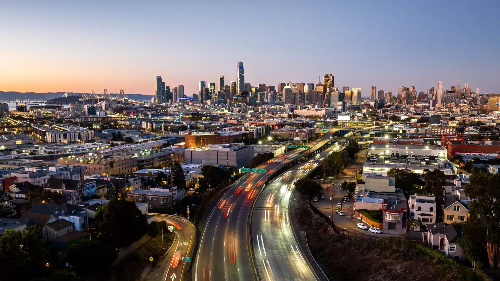 Downtown San Francisco skyline at dusk, with cars rushing on freeway heading in and out of the city.