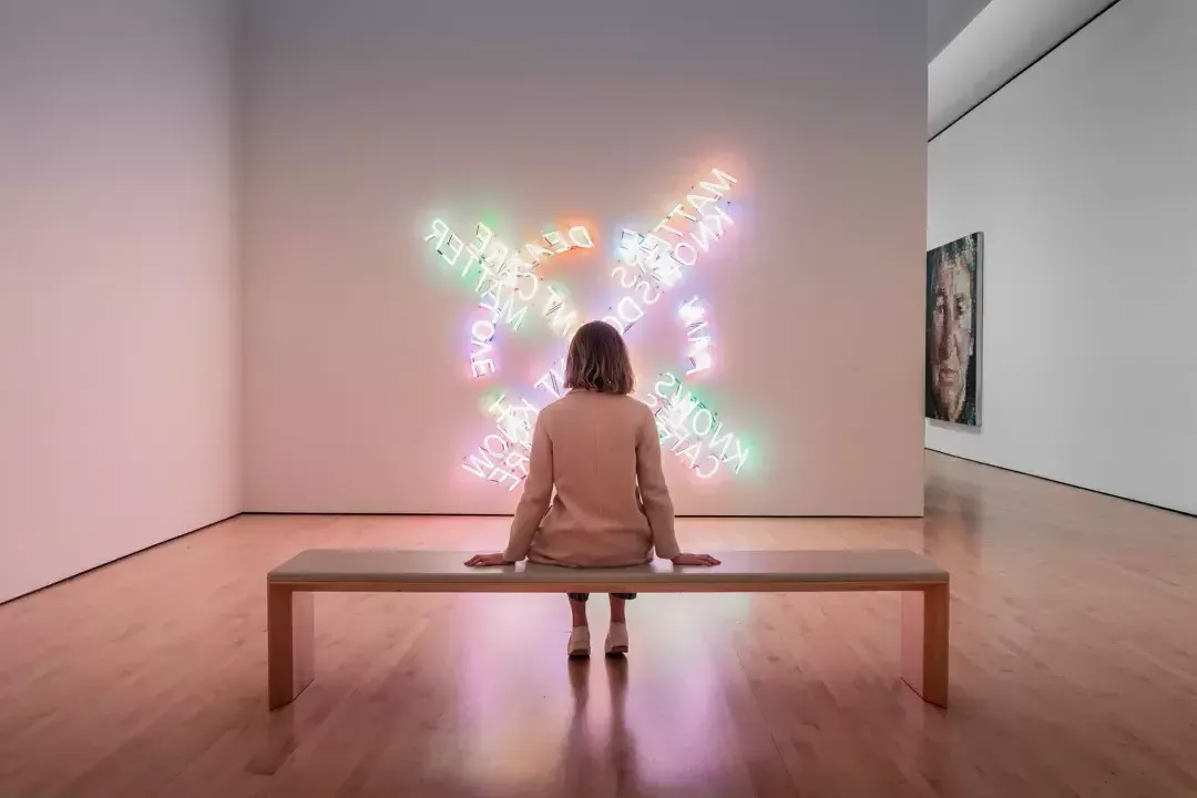 A woman, seated on a bench, looks at a piece of contemporary light art at SF MOMA in San Francisco.